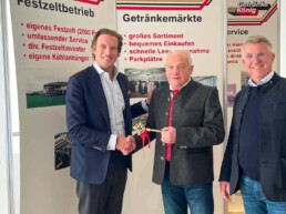 Drei Männer in dunklen Jackets stehen vor einer Getränke König Messewand